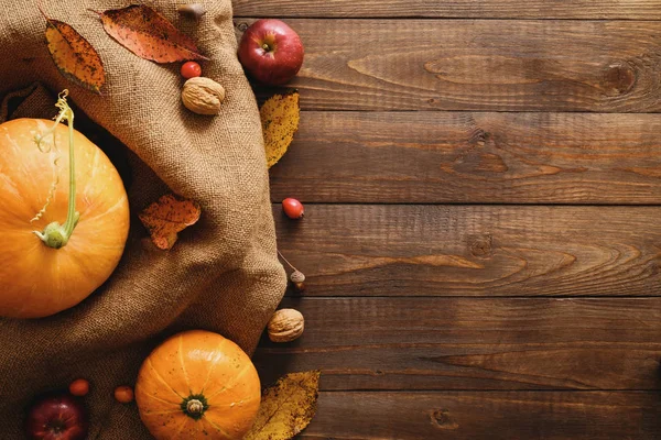 Φθινόπωρο πλαίσιο από κολοκύθες, αποξηραμένα φύλλα πτώσης, μήλα, κόκκινα μούρα, καρύδια, κουβέρτα σε ξύλινο τραπέζι. Ευχαριστίες, Απόκριες, φθινοπωρινή συγκομιδή έννοια. Επίπεδη σύνθεση, επάνω όψη, αντίγραφο χώρου — Φωτογραφία Αρχείου