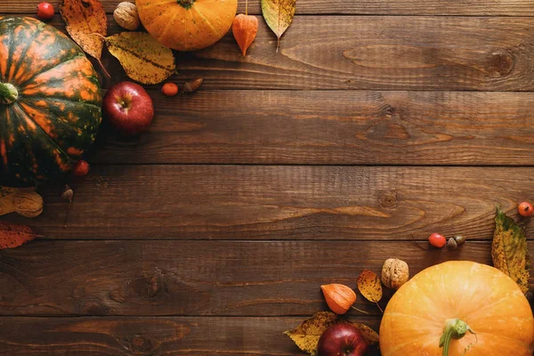 Autumn frame made of pumpkins, dried fall leaves, apples, red berries, walnuts, blanket on wooden table. Thanksgiving, Halloween, Autumn Harvest concept. Flat lay composition, top view, copy space