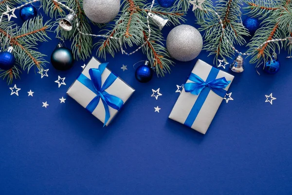 Moderní vánoční dekorace, jedlové větve, stříbrné úbory, dárkové krabice se stuhou, konfety na tmavém modrém pozadí. Veselé Vánoce a šťastný nový rok. Plochý, pohled shora. — Stock fotografie