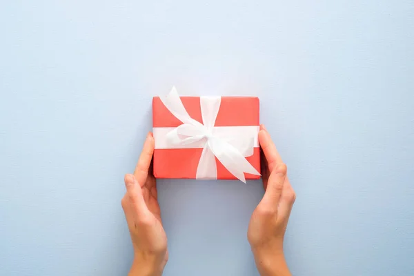 Female's hands holding red gift box with white ribbon bow on pastel blue background. Christmas, New Year, Valentine's day and birthday concept. Minimal flat lay style composition, top view, overhead — Stock Photo, Image