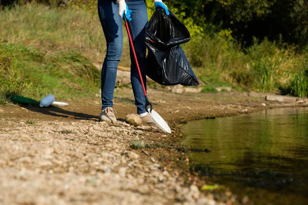 Eine freiwillige Frau sammelt Plastikmüll am Ufer des Flusses. Umweltkonzept zur Reinigung — Stockfoto