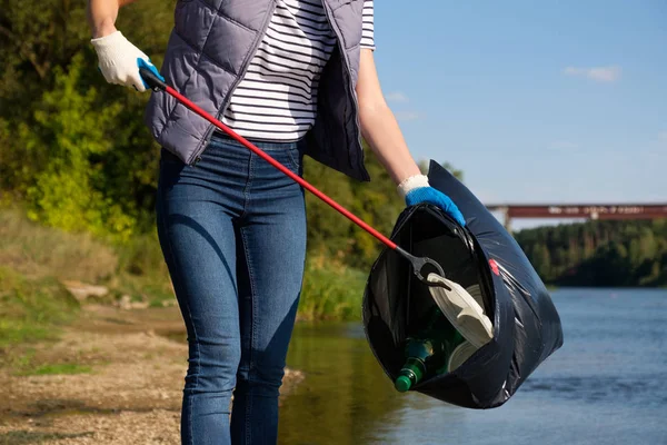 Dobrovolnická žena, která vyzvedne plastikový odpad na pobřeží řeky. Koncepce čištění prostředí — Stock fotografie