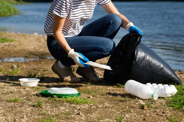 Mujer voluntaria recogiendo basura plástica en la costa del río. Concepto de ambiente de limpieza — Foto de Stock