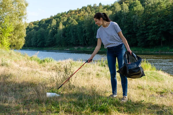 Mujer voluntaria recogiendo basura plástica en la costa del río. Concepto de ambiente de limpieza — Foto de Stock