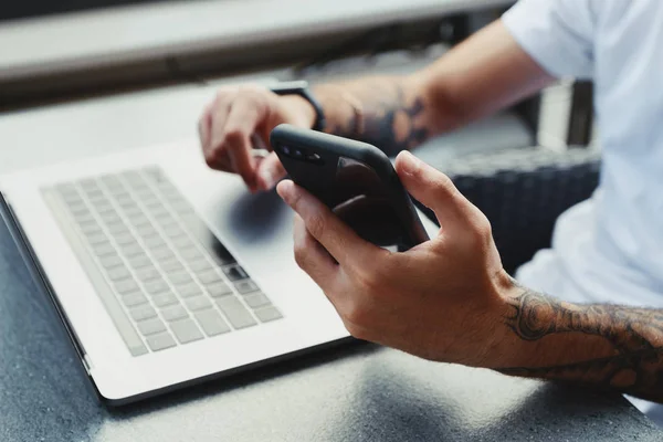 Vista ritagliata dell'uomo che lavora da casa usando smartphone e laptop. Maschio che legge messaggi di testo sul telefono cellulare, controlla e-mail, naviga in internet, guarda video sul telefono cellulare in caffetteria — Foto Stock