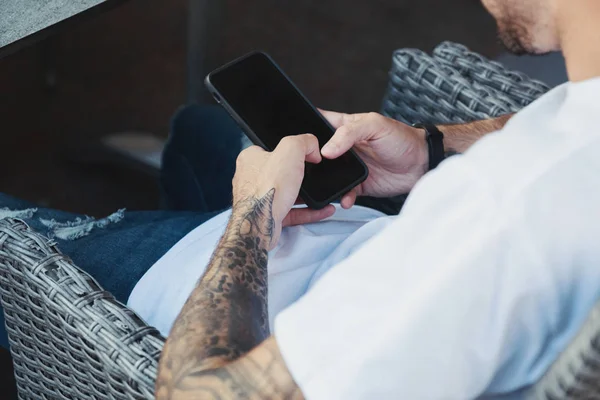 Close-up mannelijke handen met Tattoo houden smartphone met lege kopie ruimtescherm tijdens het verbinden met 4G draadloos of WiFi-netwerk, hipster kerel met behulp van technologie zittend in moderne coffeeshop. — Stockfoto