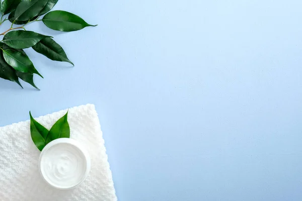 Herbal dermatology cosmetic hygienic cream with green leaf skincare product in glass jar on blue background. Flat lay, top view, overhead. Skin care, beauty and healthcare concept.