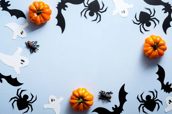 Happy halloween holiday concept. Halloween decorations, spiders, bats, ghosts, pumpkins on blue background. Halloween party greeting card mockup with copy space. Flat lay, top view, overhead.