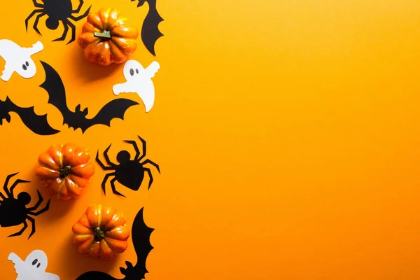 Happy halloween holiday concept. Halloween decorations, spiders, pumpkins, bats, ghosts on orange background. Halloween party greeting card mockup with copy space. Flat lay, top view, overhead.