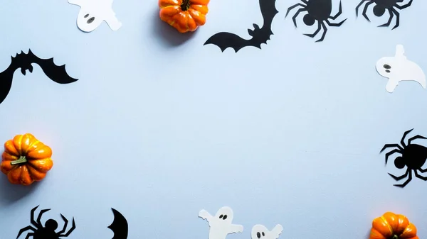 Happy halloween holiday concept. Halloween decorations, ghosts, pumpkins, bats, spiders on blue background. Halloween party banner mockup with copy space. Flat lay, top view, overhead.
