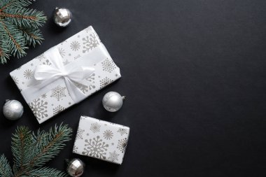 Gümüş kağıda sarılı hediye kutuları ve siyah arka planda dekoratif toplarla süslenmiş köknar ağacı dalları. Noel afişi, yeni yıl kartpostal şablonu. Düz yatıyordu, üstten, yukarıdan.