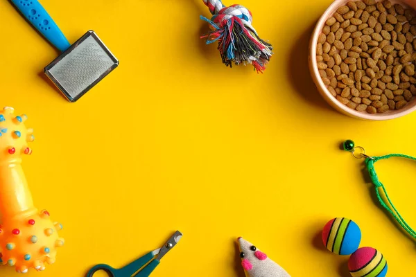 Flat lay composition with pet accessories and bowl of dry food on yellow background. Pet care and training concept.