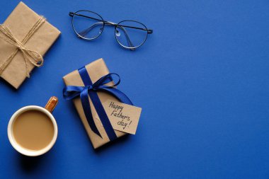 Babalar Günün kutlu olsun. Mutlu Babalar Günü yazıları, mavi arka planda bir fincan kahve ve bardaklar olan düz kompozisyon. Üst görünüm.