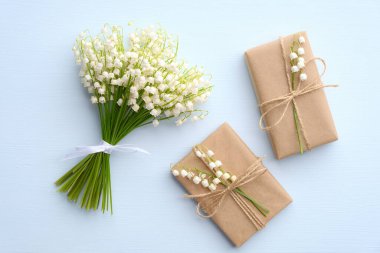 Çiçek buketi vadi zambağı ve mavi masaya sarılı iki hediye kutusu, yukarıdan manzara. Anneler Günü ya da Kadınlar Günü hediyeleri.