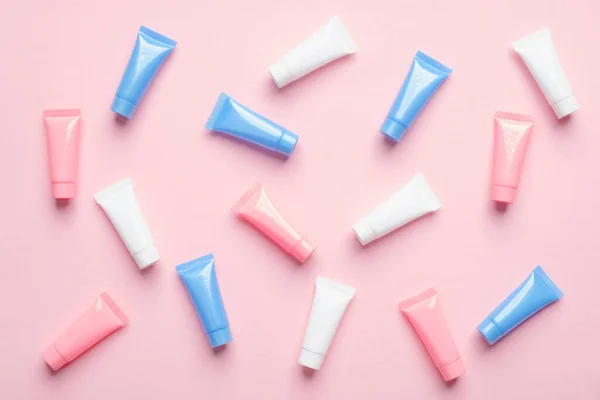 Many colorful cosmetic tubes on pink background. Blank plastic beauty products packaging. Flat lay, top view.