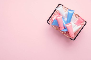 Pembe arka planda renkli kozmetik tüplerle dolu alışveriş sepeti. Kozmetik mağazası afiş tasarımı. Düz yatış, üst görünüm