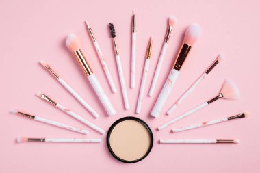 Profesyonel makyaj fırçaları ve pembe arka planda pudra ile yaratıcı düz kompozisyon. Üst görünüm.
