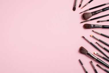 Pembe arka planda farklı siyah makyaj fırçaları. Düz yerde, üst tarafta. Makyaj dükkanı afiş tasarımı.
