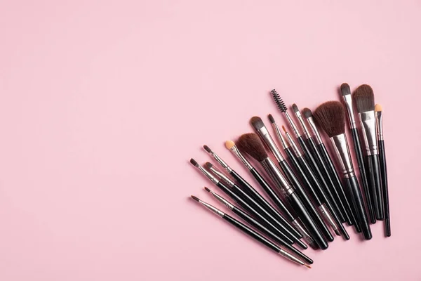 Set of black professional makeup brushes on pink background. Flat lay, top view. Makeup shop banner design.