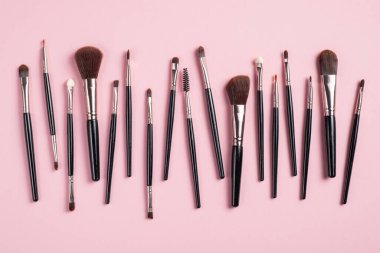 Makyaj fırçaları pembe arka planda izole edilmiş. Yaratıcı düz konum biçimi, üst görünüm. Moda makyaj ürünleri seti