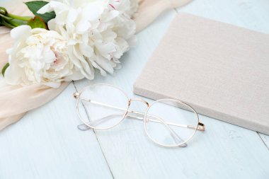 Gözlükler, kağıt defter ve şakayıklar mavi ahşap masada. Şık düğün aksesuarları üst görünüm.