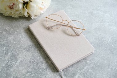 Kağıt defter, bardaklar, taş zeminde şakayık çiçeklerle bezenmiş düz bir kompozisyon. Moda kızı çalışma alanı konsepti.