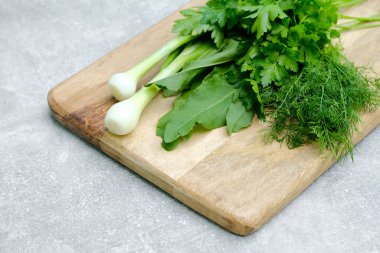 Taze çiğ, sağlıklı organik yiyecekler, ahşap kesim tahtasındaki salata malzemeleri. Yeşil soğan, maydanoz, dereotu, doru