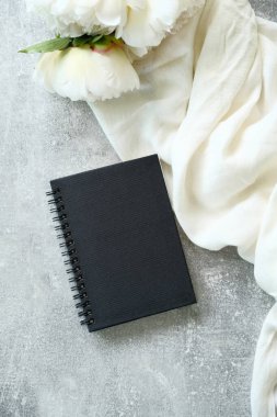 Üzerinde bej kumaş ve taştan arka planda şakayık çiçekleri olan siyah kağıt bir defter. Üst manzara, düz uzanma.