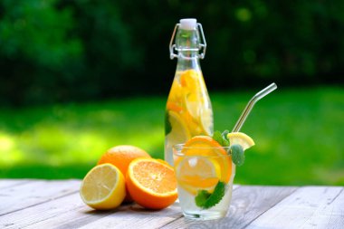 Portakal dilimleri ve nane şekeri ile karıştırılmış meyve suyu ve kırsal ahşap masa üzerinde cam ve şişe. Serinletici yaz içeceği, organik kokteyl