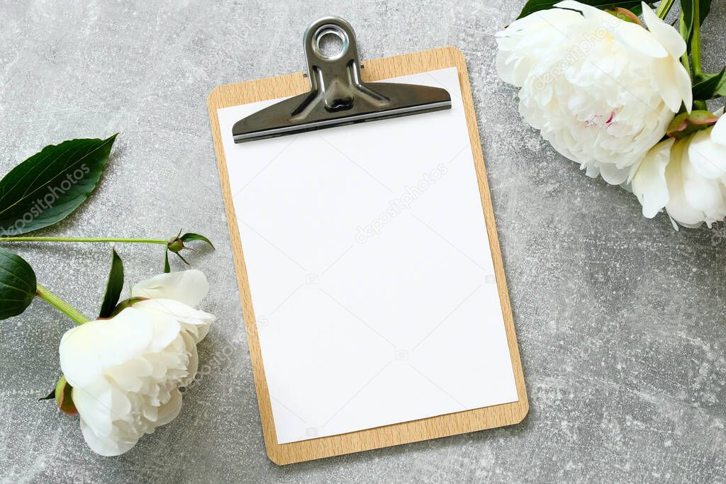 Flat lay style wedding composition with blank sheet clipboard mockup and peony flowers on stone table. Top view.