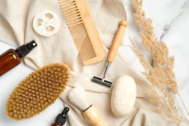 Mermer arka planda bej kumaşlı ve kuru çiçekli erkekler için çevre dostu banyo aksesuarları. Tıraş fırçası, jilet, vücut fırçası, kozmetik şişesi, sabun, lif lifi, ahşap saç tarağı..