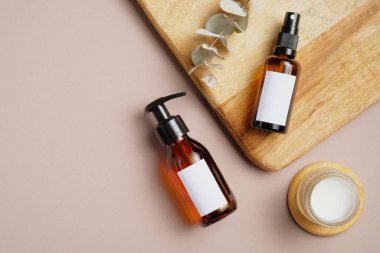 Bej arka planda SPA doğal organik kozmetik ürünleri. Kehribar cam pompa şişesi, sprey, nemlendirici krem kavanozu, okaliptüs yaprağı ile düz kompozisyon. Üst görünüm.