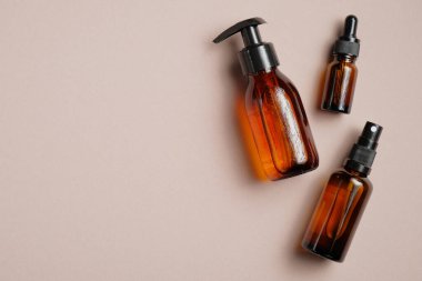 Kahverengi arka planda kehribar cam kozmetik şişeleri. Pompa şişesi, damlalık şişesi, dağıtıcı kozmetik konteynır düz, üst görünüm.