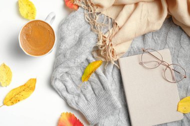 Sonbahar kompozisyonu. Bir fincan kahve, gri kazak, bej kadın atkısı, düşmüş yapraklar, kağıt defter, beyaz arka planda gözlük. Sonbahar, sonbahar konsepti. Düz yatış, üst görünüm.