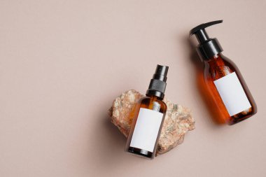 SPA doğal organik kozmetik ambalaj tasarımı. Kehribar cam sprey şişesi vücut losyonu ve şampuan şişesi bej arka planda taşlı maket..