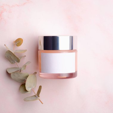 Nemlendirici kremalı kavanoz ve pembe arka planda okaliptüs yaprağı. Kozmetik ürün ambalaj tasarımı, kabın modeli