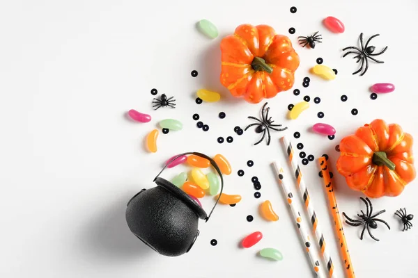 Happy halloween holiday concept. Halloween decorations, pot with sweet candies, orange pumpkins, spiders, confetti on white background. Halloween party greeting card mockup. Flat lay, top view.
