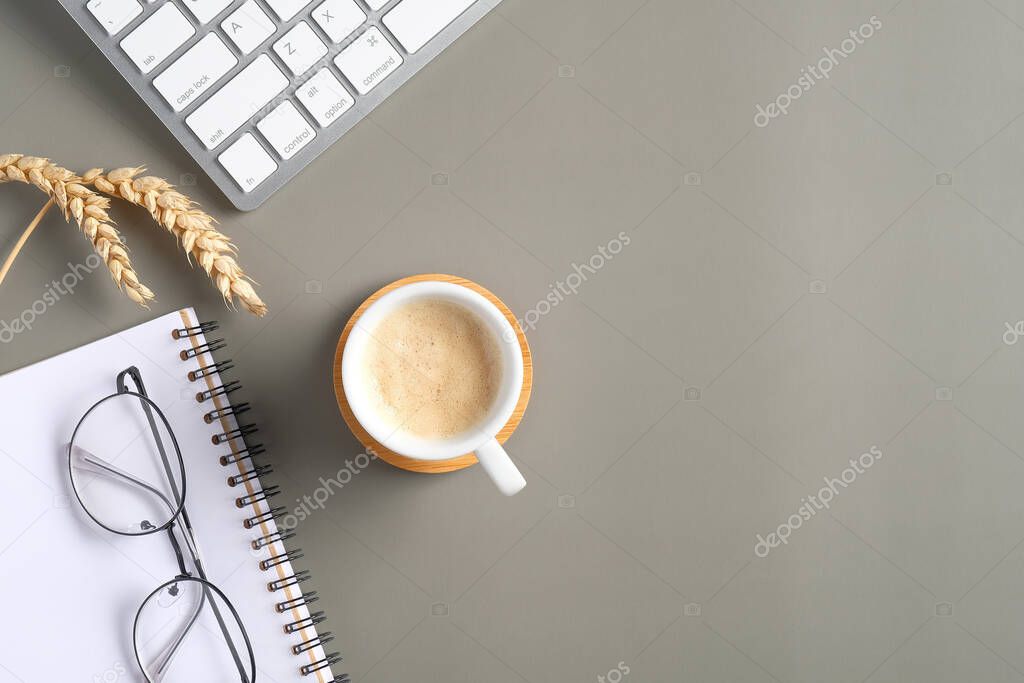 Modern office desk table with coffee cup, computer keyboard, paper notebook, glasses, wheat on green background. Flat lay, top view, overhead.
