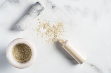 Ubtan doğal yüz yıkama kozmetik hazırlığı. Ubtan pudrası ve mermer masanın üzerinde güzellik ürünü şişesi olan bir kase. Düz yatış, üst görünüm.