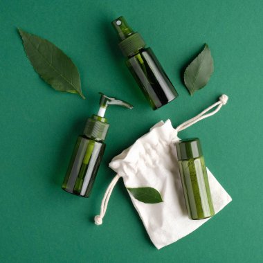 Sıfır atık kozmetik set. Düz bir zemin, yeşil kozmetik şişeleri, bitki yaprakları ve yeşil arka planda çanta. SPA doğal organik güzellik ürünleri.