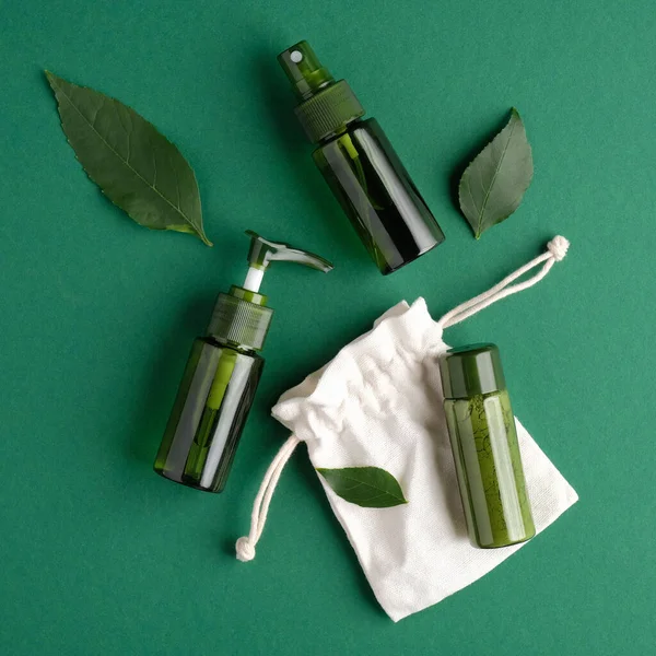 Sıfır atık kozmetik set. Düz bir zemin, yeşil kozmetik şişeleri, bitki yaprakları ve yeşil arka planda çanta. SPA doğal organik güzellik ürünleri.