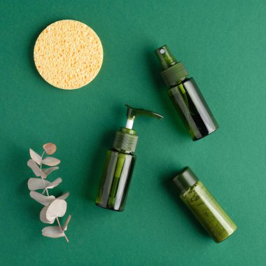 Düz bir zemin, yeşil kozmetik şişeleri, sünger, yeşil arka planda okaliptüs yaprağı. Doğal organik güzellik ürünleri seti. Güzellik ve güzellik konsepti.