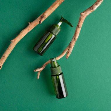 Çevresel doğal kozmetik şişesi seti ve yeşil arka planda ahşap dal. Organik güzellik ürünleri ambalaj tasarımı. Düz yatış, üst görünüm.