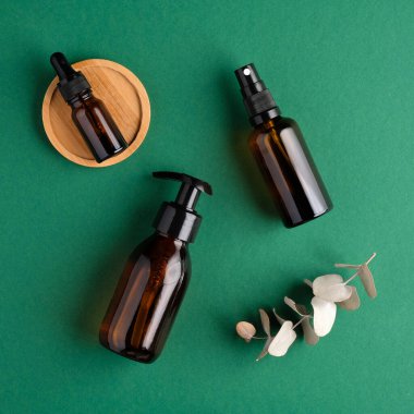 SPA doğal organik kozmetik seti. Yeşil arka planda kehribar cam şişeler ve okaliptüs yaprağı. Düz yerde, üst tarafta. Cilt bakımı kavramı.