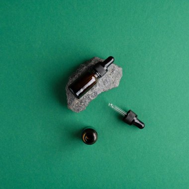 Yeşil arka planda serum düşürücü şişesi ve taş. Düz yerde, üst tarafta. Doğal organik kozmetik konsepti.