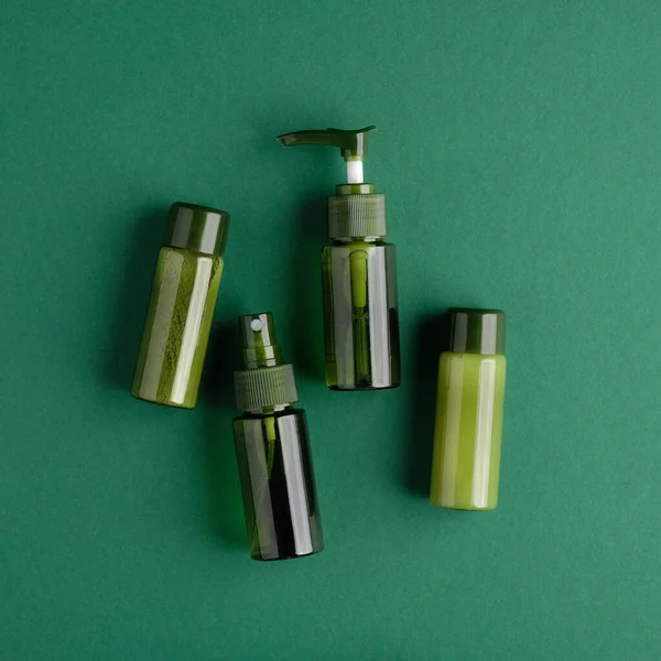 Green cosmetic bottles set on green background. Bio organic beauty product, natural cosmetic packaging design. Flat lay, top view.