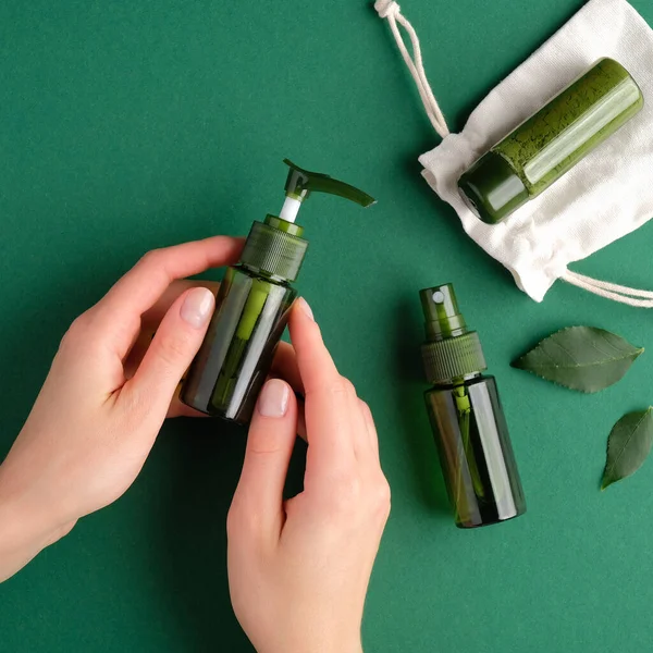 Kozmetik yeşil tulumbayı doğal organik güzellik ürünleriyle dolu bir masanın üzerinde tutan kadın elleri. Düz yerde, üst tarafta. Cilt bakımı için SPA el kremi.
