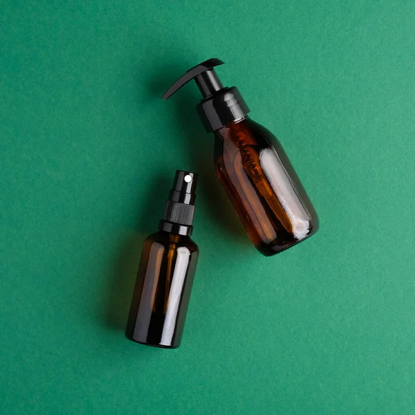 Cosmetic amber glass bottles on green background. Flat lay, top view. Natural organic beauty products packaging design.
