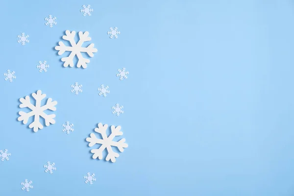 Christmas composition. Frame border of white snowflakes and confetti on blue background. Flat lay, top view, minimal style.