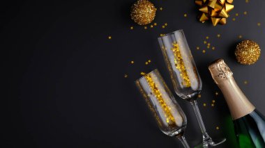 Modern Noel partisi konsepti. Şarap kadehli şampanya şişesi, altın konfeti, siyah arka planda toplar. Lüks düz kompozisyon, üst görünüm.